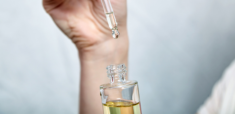 Hand using a dropper to extract organic essential oil from a glass bottle, emphasizing purity and precision. Suitable for content about aromatherapy or skincare routines